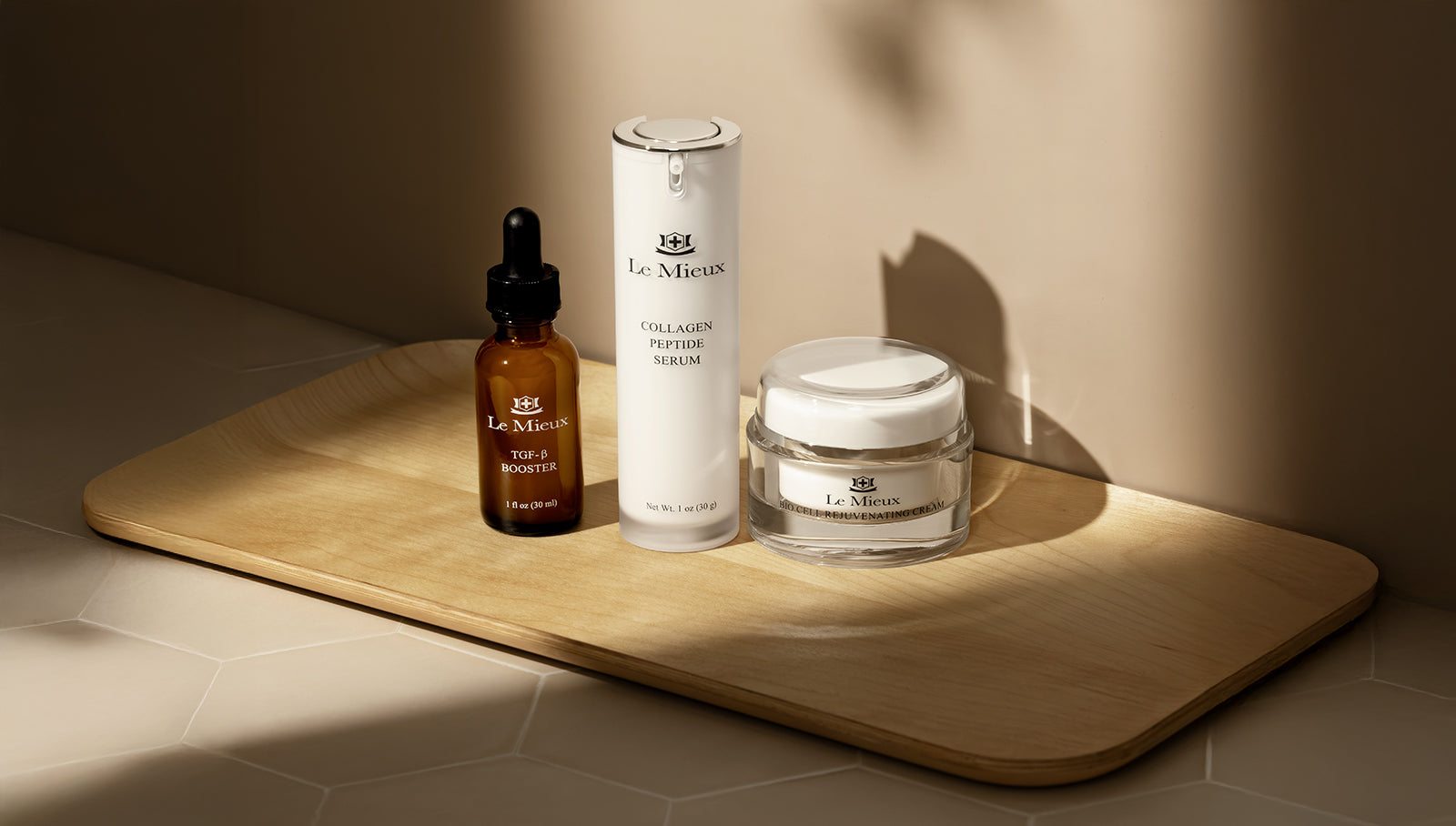 trio of skincare products (two serum bottles and a cream jar) on a bamboo tray on a tiled floor against a clean wall 